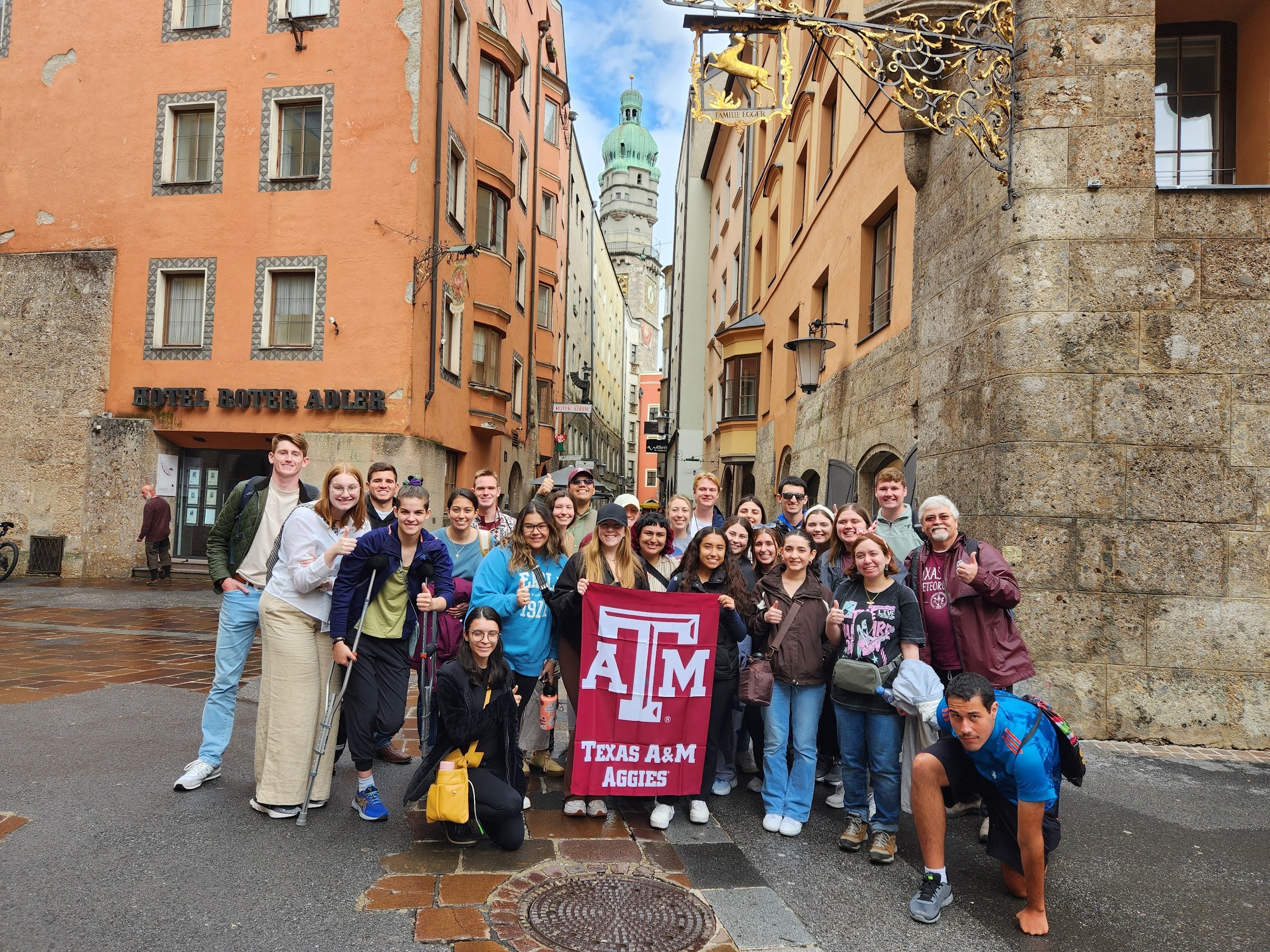 Texas A&M University students participating in the 2023 Student Experiences Abroad in Meteorology program pose with a maroon Texas A&M University flag on a street corner in Munich, Germany