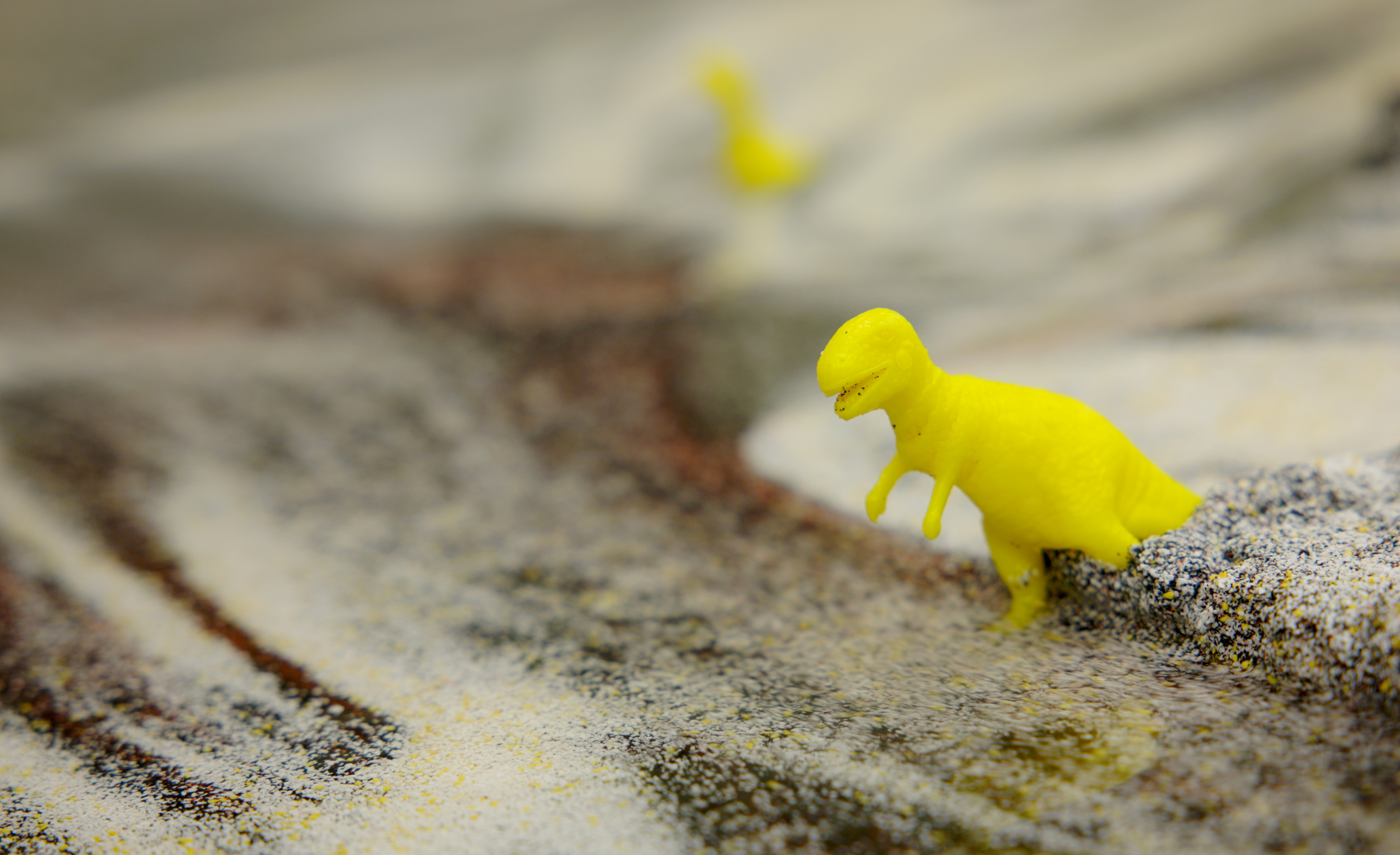 Close-up of a toy dinosaur in multicolored sand within the model landscape of a stream table in the Texas A&amp;M University Department of Geology and Geophysics