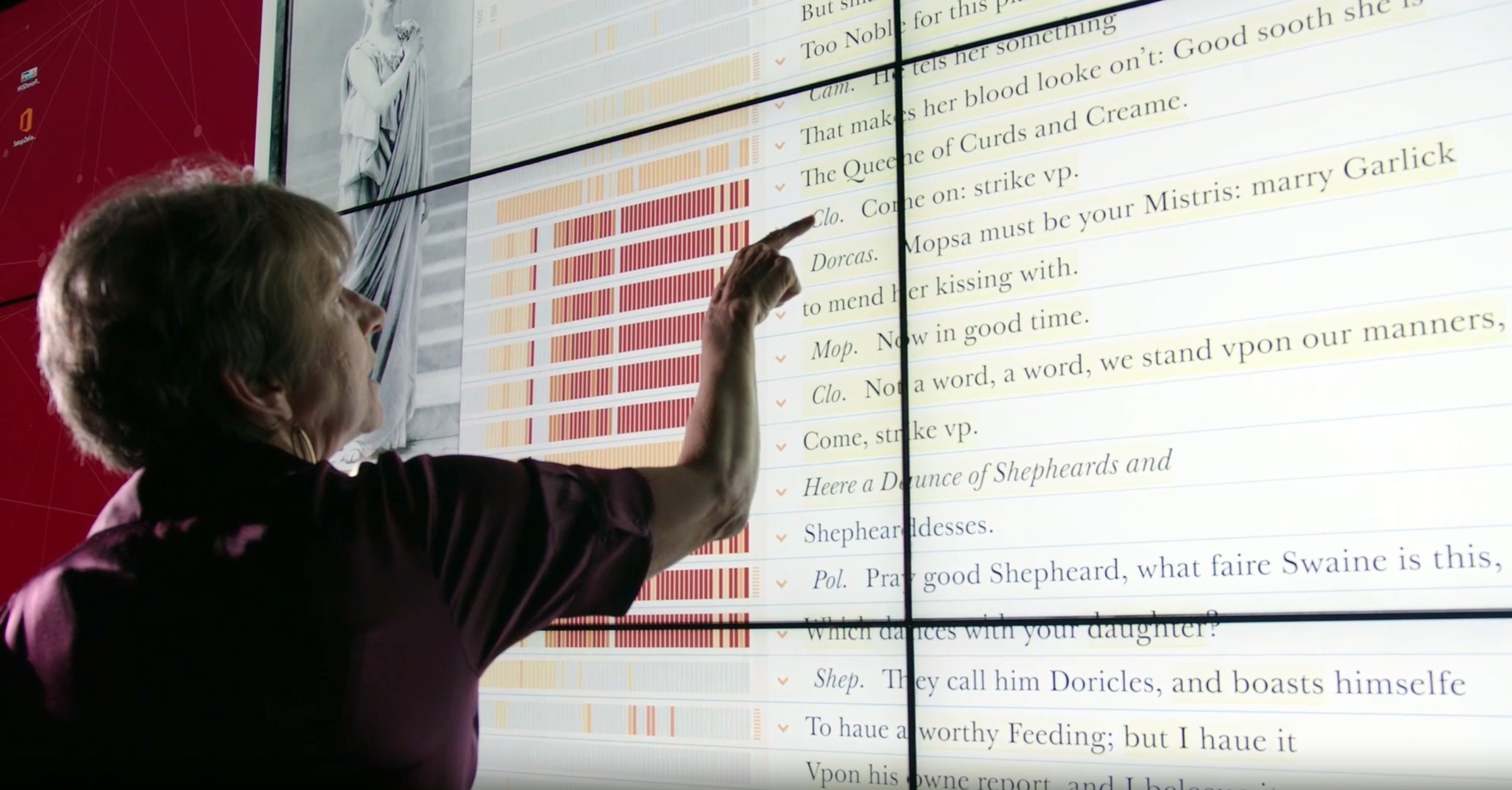 Texas A&amp;M University English Professor Laura Mandell extends her index finger toward a wall-sized touch-screen display featuring the New Variorum Shakespeare website in the Humanities Visualization Space within the Center of Digital Humanities Research