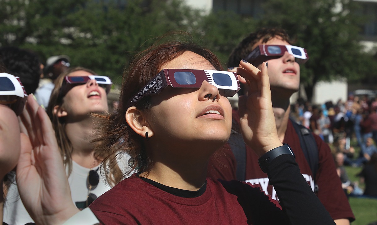 A group of Texas A&amp;M University students look skyward while wearing Texas A&amp;M-branded maroon and white eclipse glasses during the partial solar eclipse on October 14, 2023