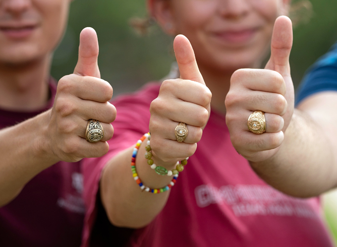 Close-up of three Texas A&amp;M University students flashing gig 'ems for the camera with their Aggie Rings prominently displayed