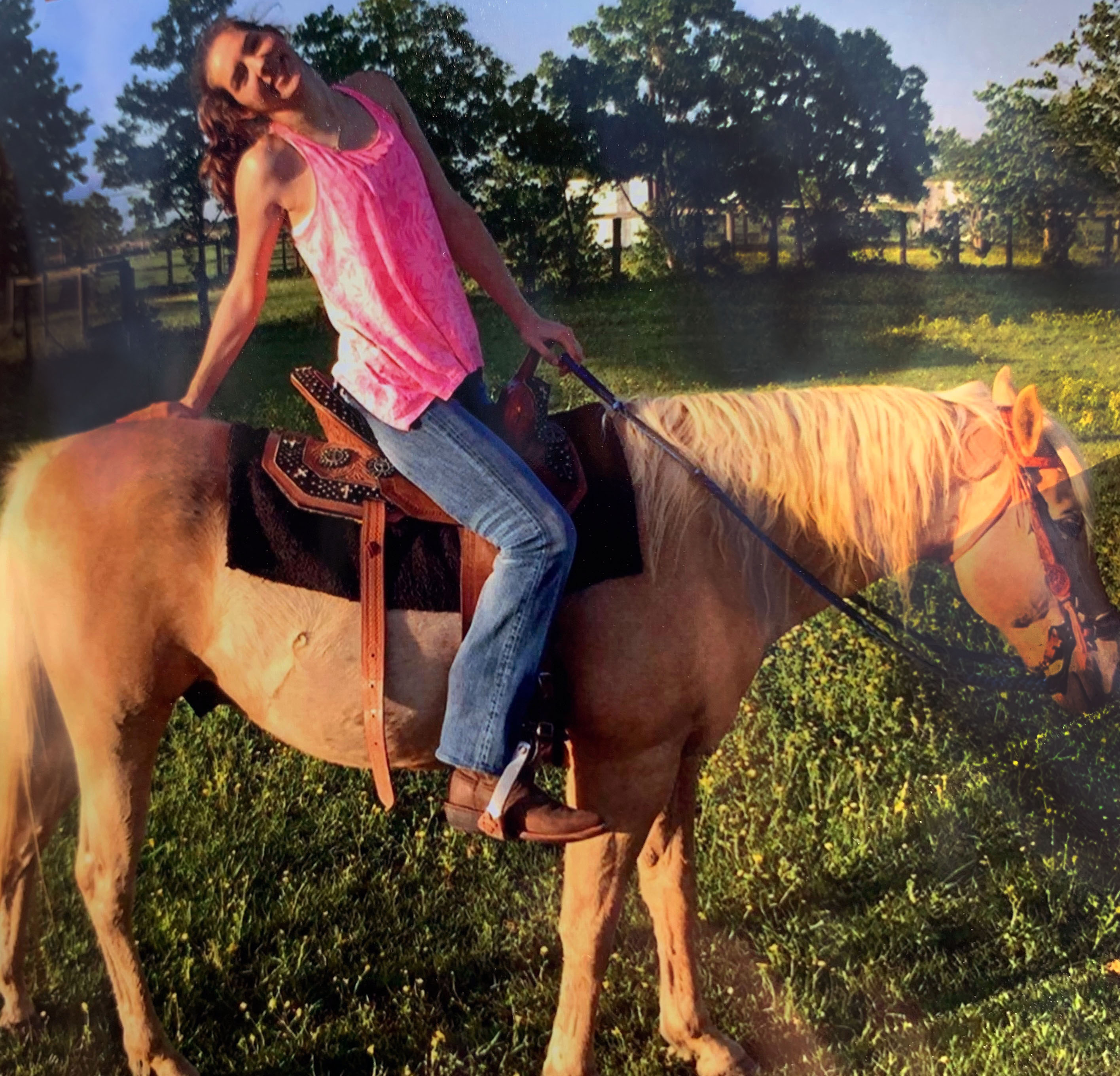 Hannah Joy Boothe sits atop a palomino horse, smiling for the camera on a sunny day in a green pasture setting