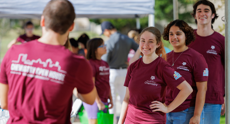 Department of Chemistry staff and students smile while manning the welcome table at the 2023 Chemistry Open House