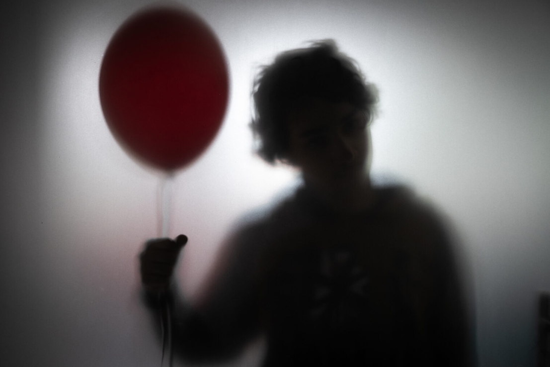 The evil clown Pennywise appears in silhouette, holding his trademark red balloon against a smoky white background