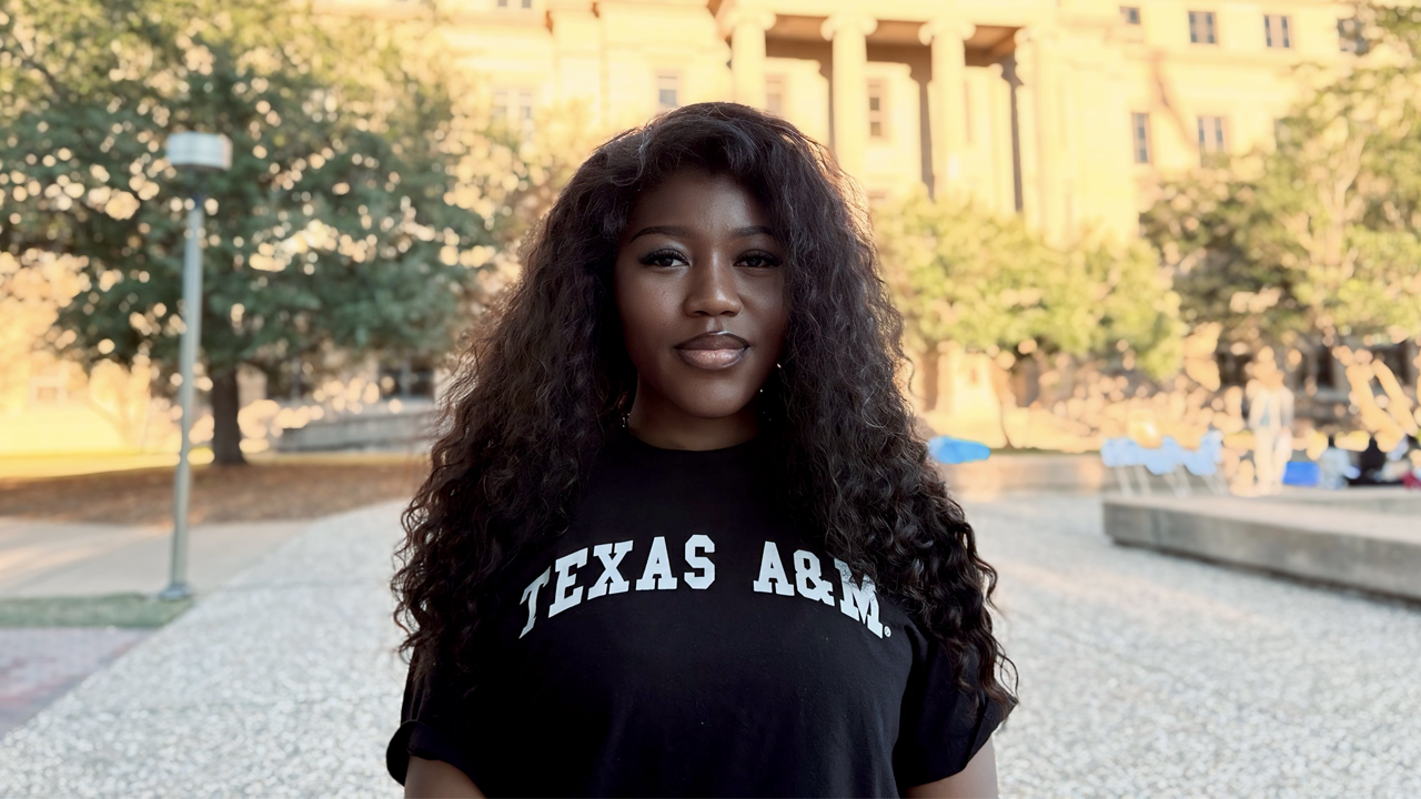 Jewel Fanyui wearing a Texas A&amp;M T-shirt, standing in front of the Academic Building on the campus of Texas A&amp;M University.