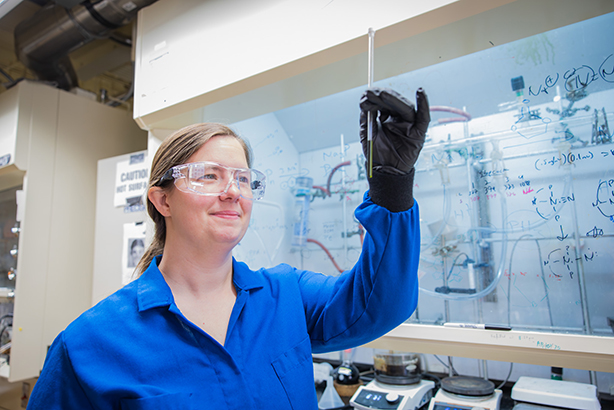 A girl in a lab coat smiles at a test tube in a lab