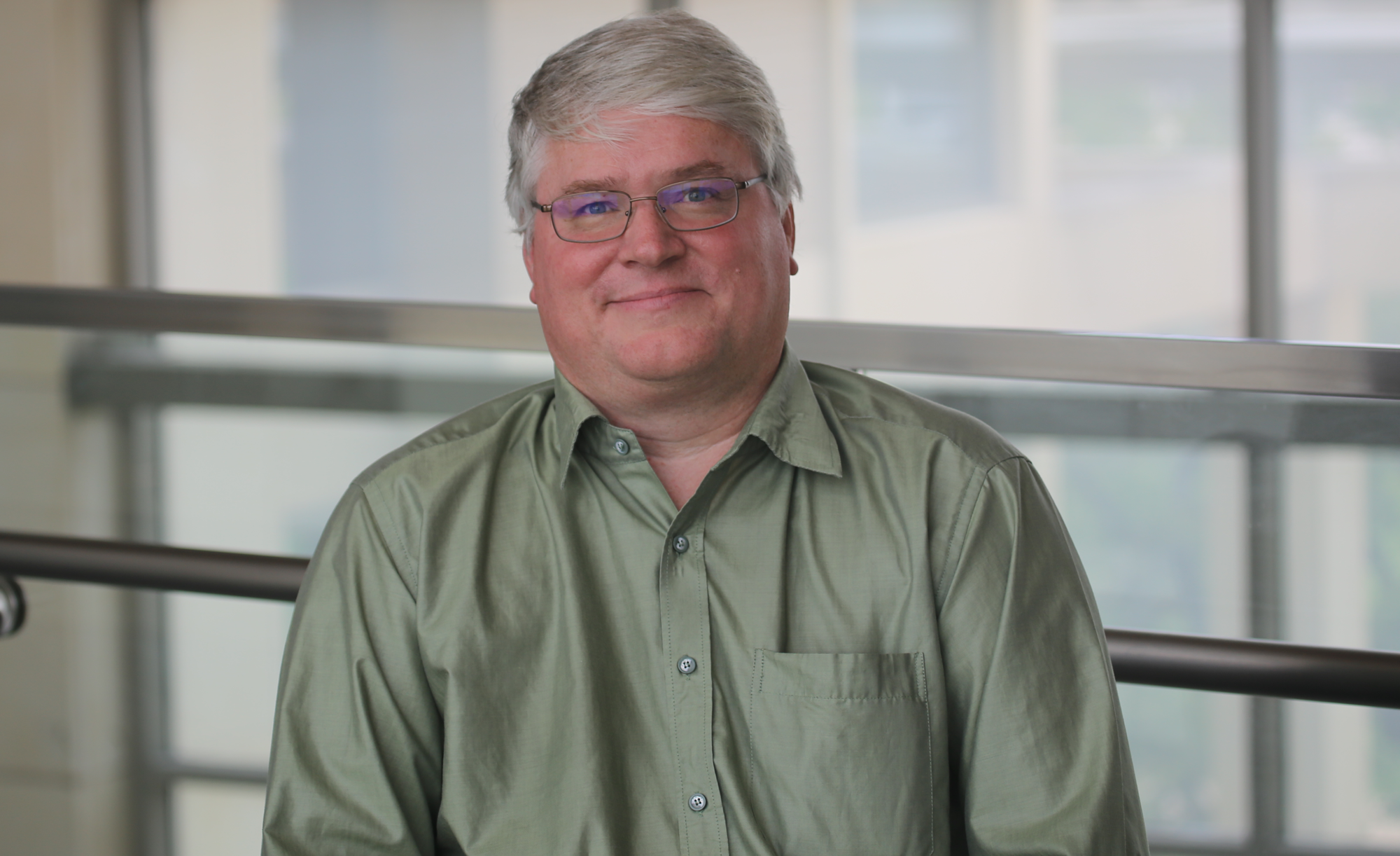 Dr. James Smith in an olive button down smiling in front of a sunny window