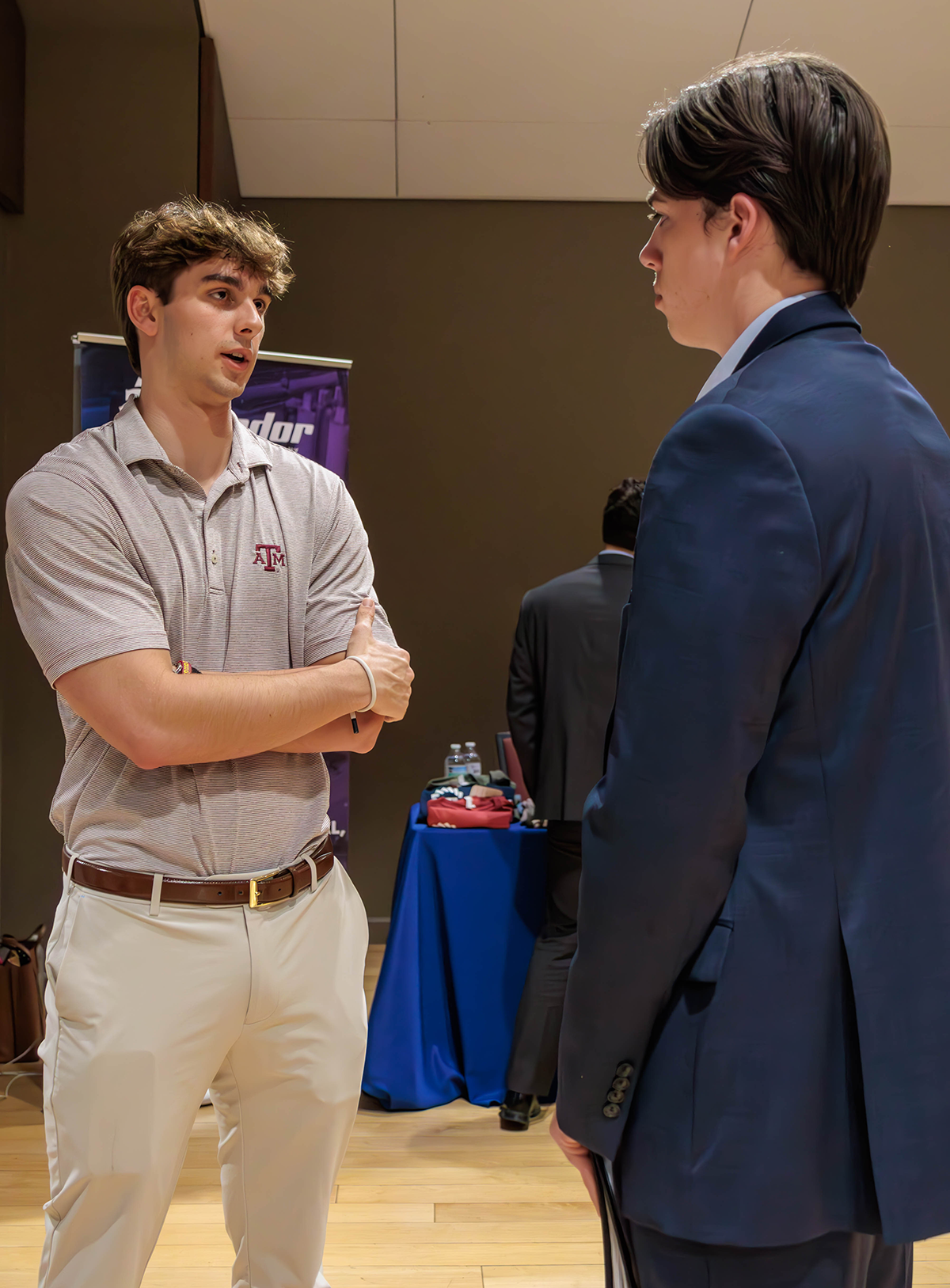 A representative from Matador dressed in a Texas A &amp; M polo speaks with a student dressed in a suit.