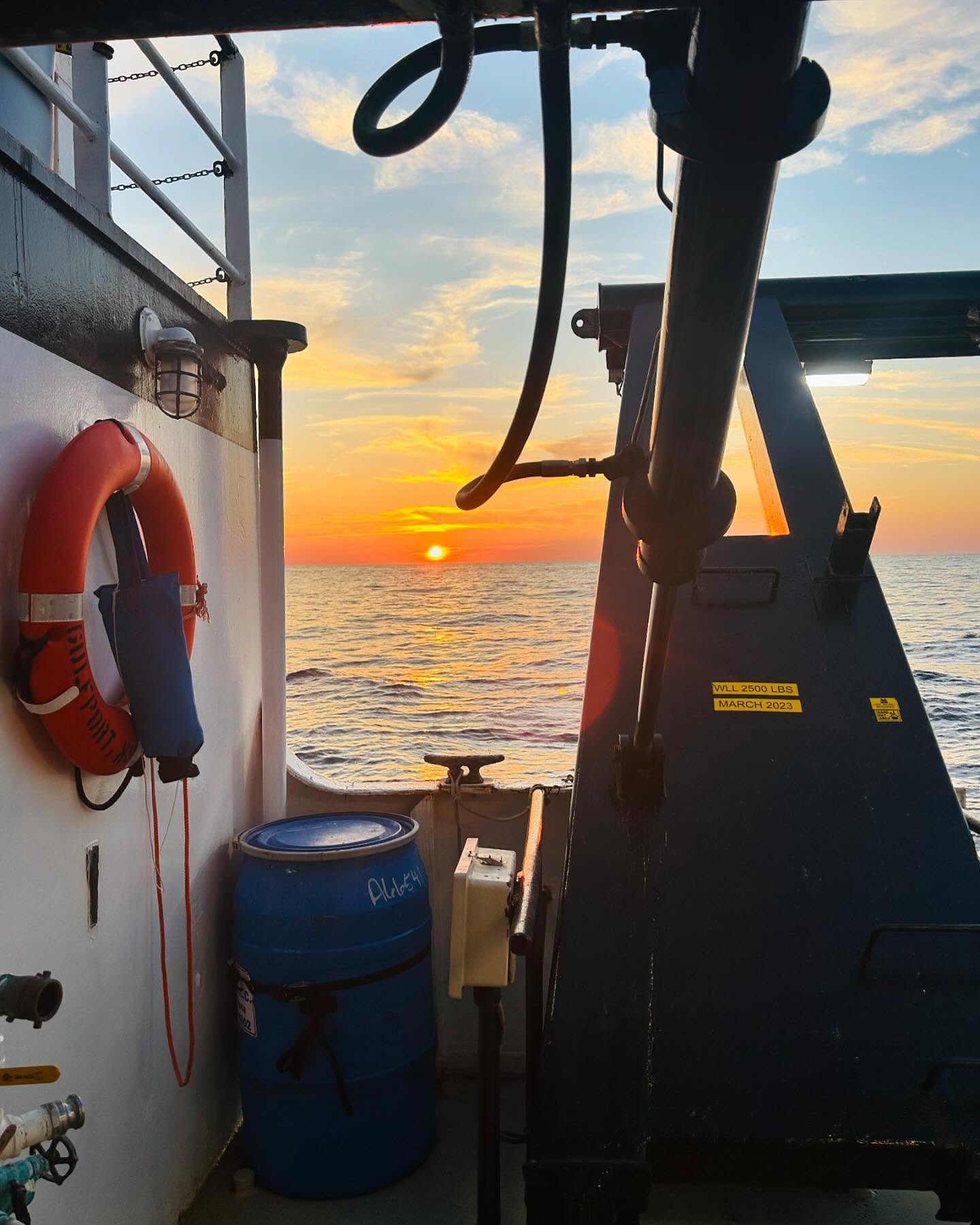 Sunset view from the deck of a boat, featuring safety equipment and a clear sky.