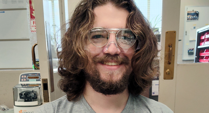 Texas A&amp;M University physics graduate student Ryan Amberger, wearing goggles and smiling while in a laboratory at Argonne National Laboratory in 2024.