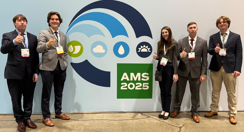 Five individuals posing with thumbs up in front of an AMS 2025 conference banner.