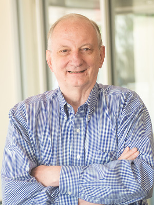 Ed Fry, wearing a blue and white striped shirt, stands smiling with his arms crossed.