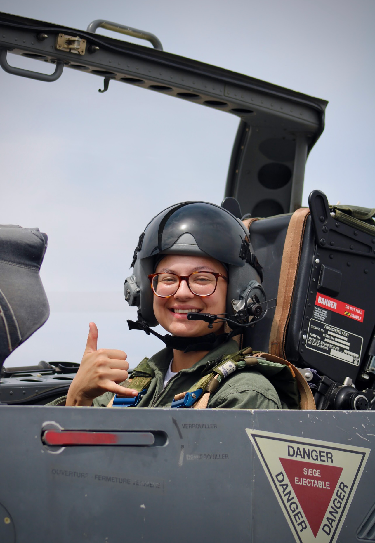 Chloe Hoercher in an aviation helmet and headset giving a thumbs up while seated in the cockpit of a military aircraft.