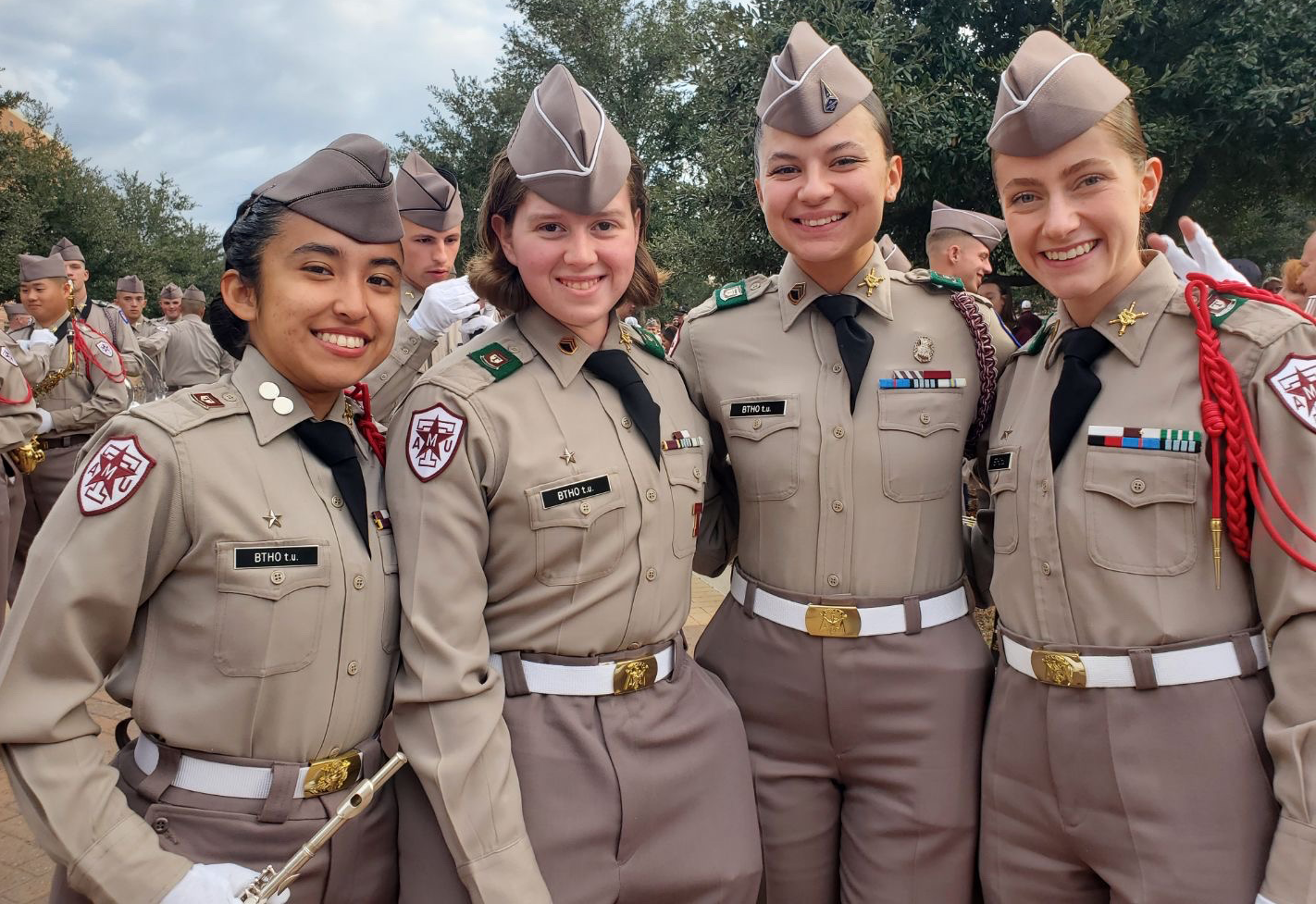 Four band members in dress uniforms smiling at a pregame event.