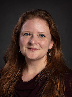 Headshot of Cecilia Emmelhainz, wearing a black top, against a black backdrop.