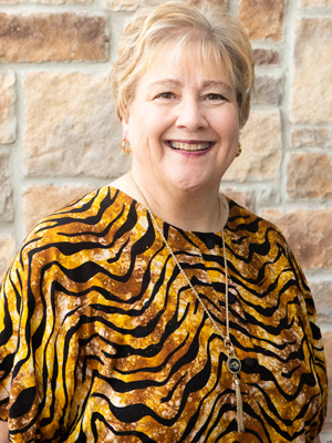 Lynn Hagan, wearing an animal-print top, poses in front of a rock wall, smiling.