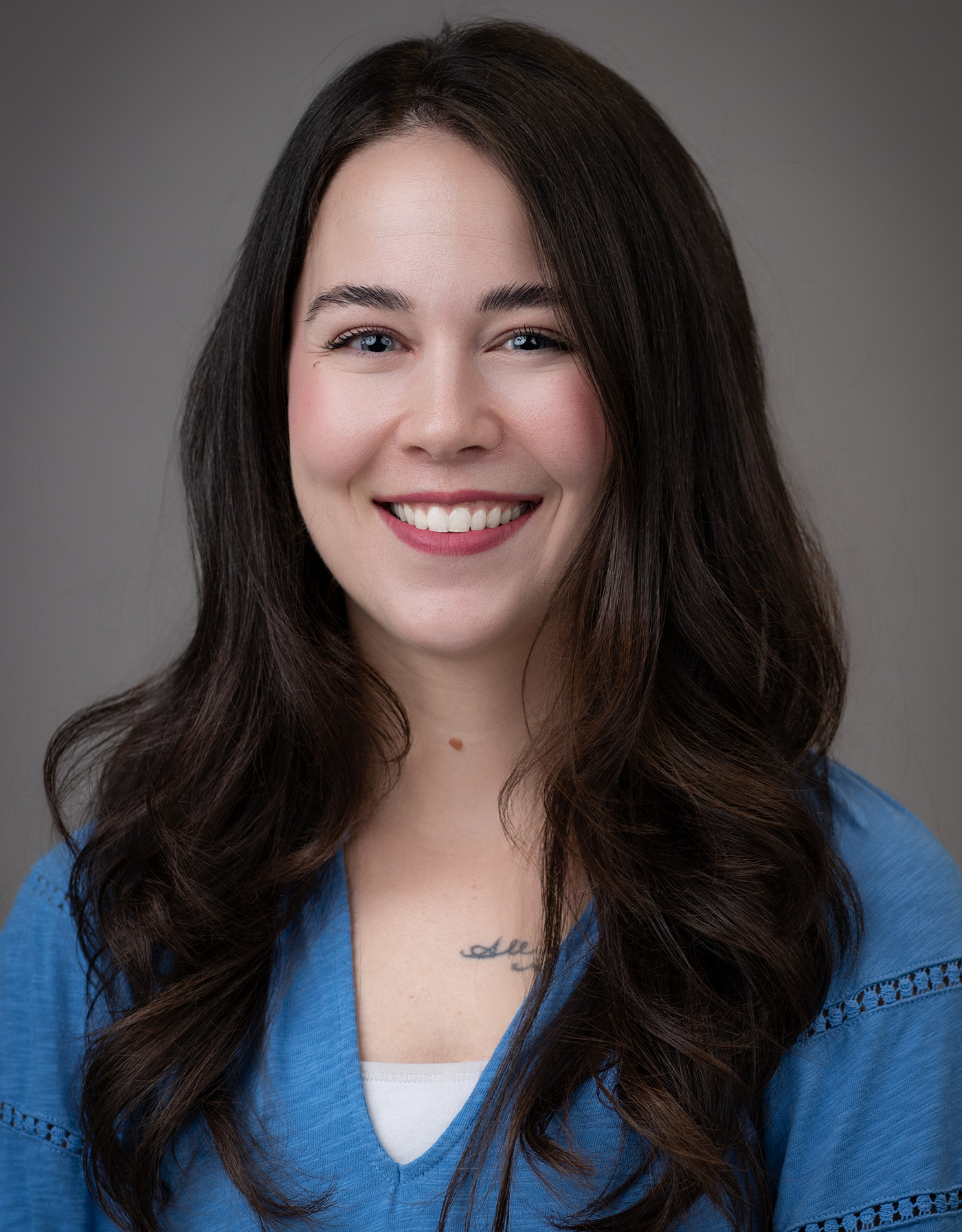 Portrait of a smiling Kaitlin Tindel with long brown hair, wearing a blue top.