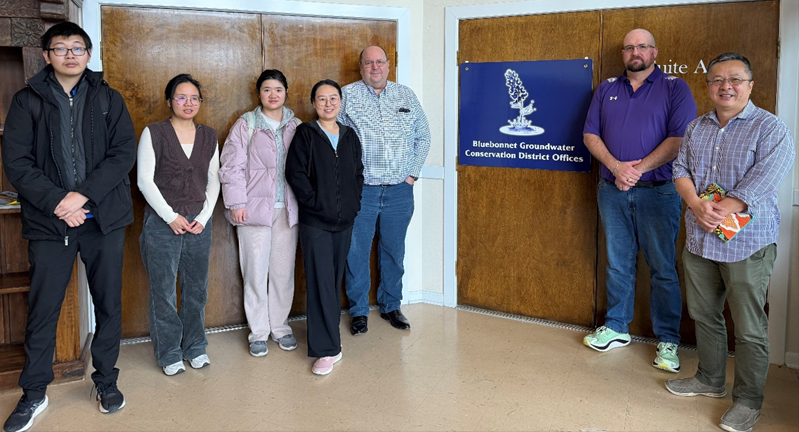 Seven people standing in a line inside an office next to a sign that reads Bluebonnet Groundwater Conservation District Offices.