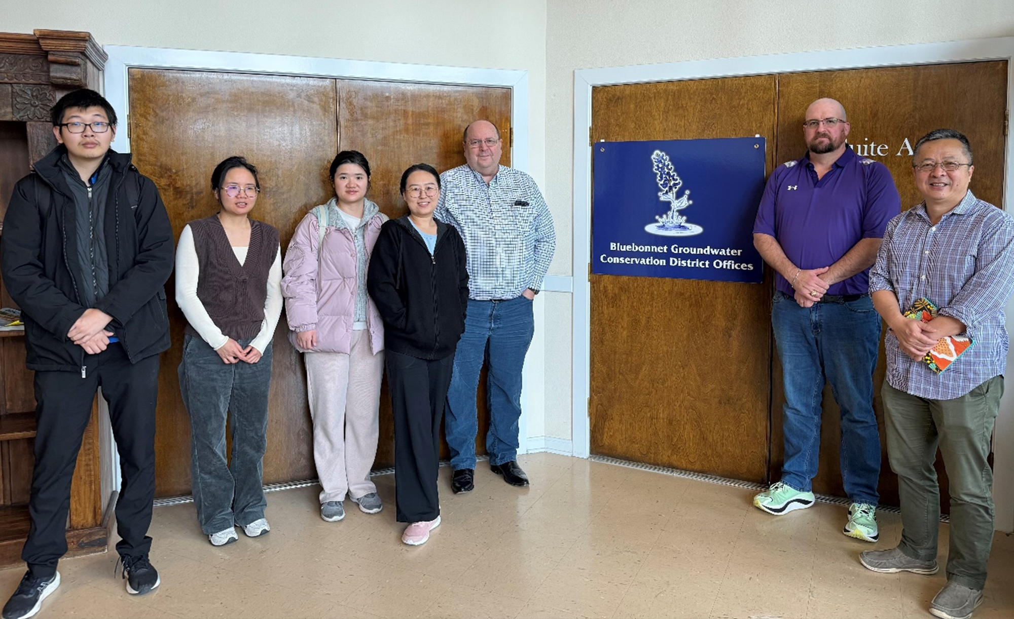 Seven people standing in a line inside an office next to a sign that reads Bluebonnet Groundwater Conservation District Offices.