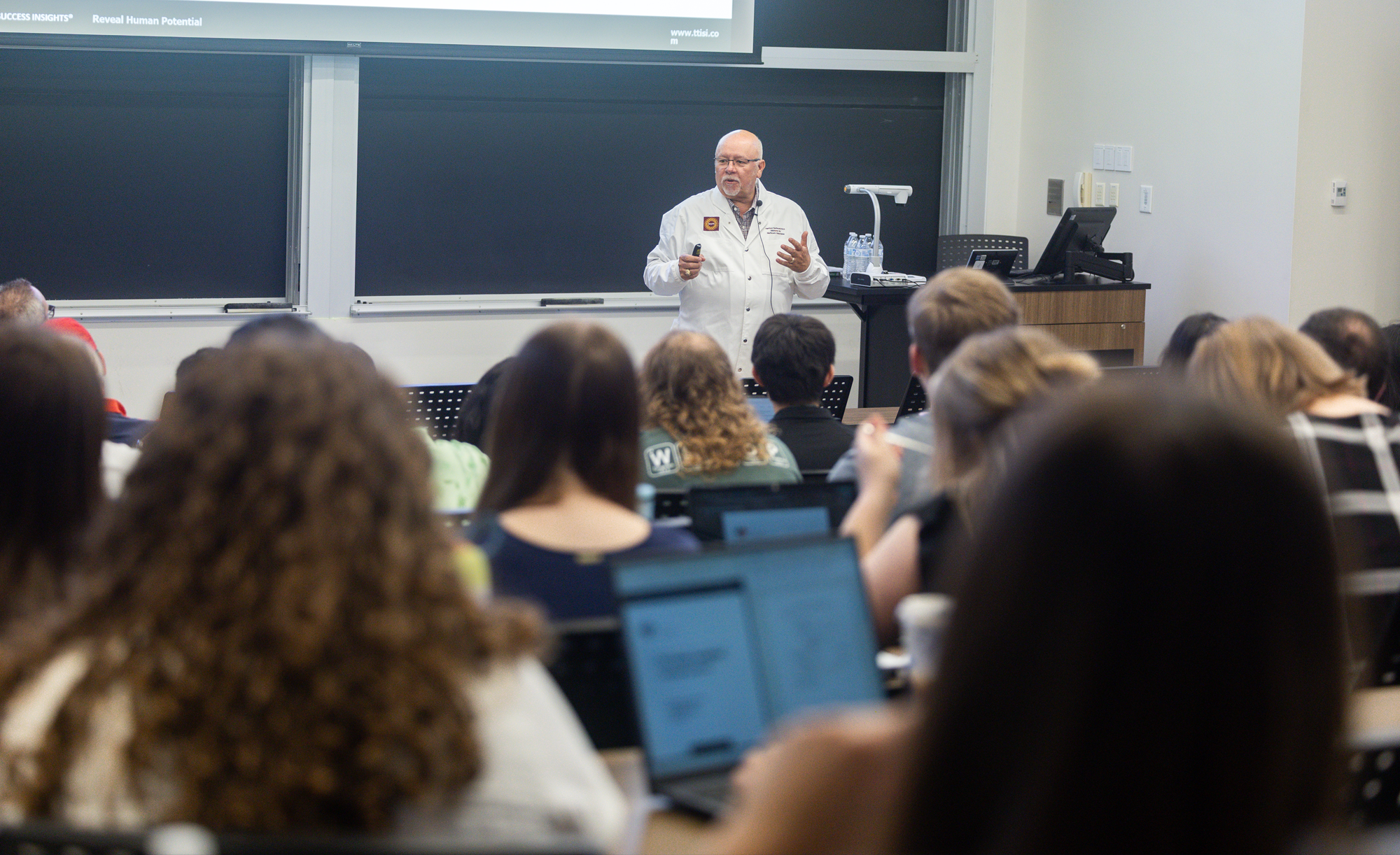 Dr. Harthcock is giving a lecture to a classroom full of attentive students.