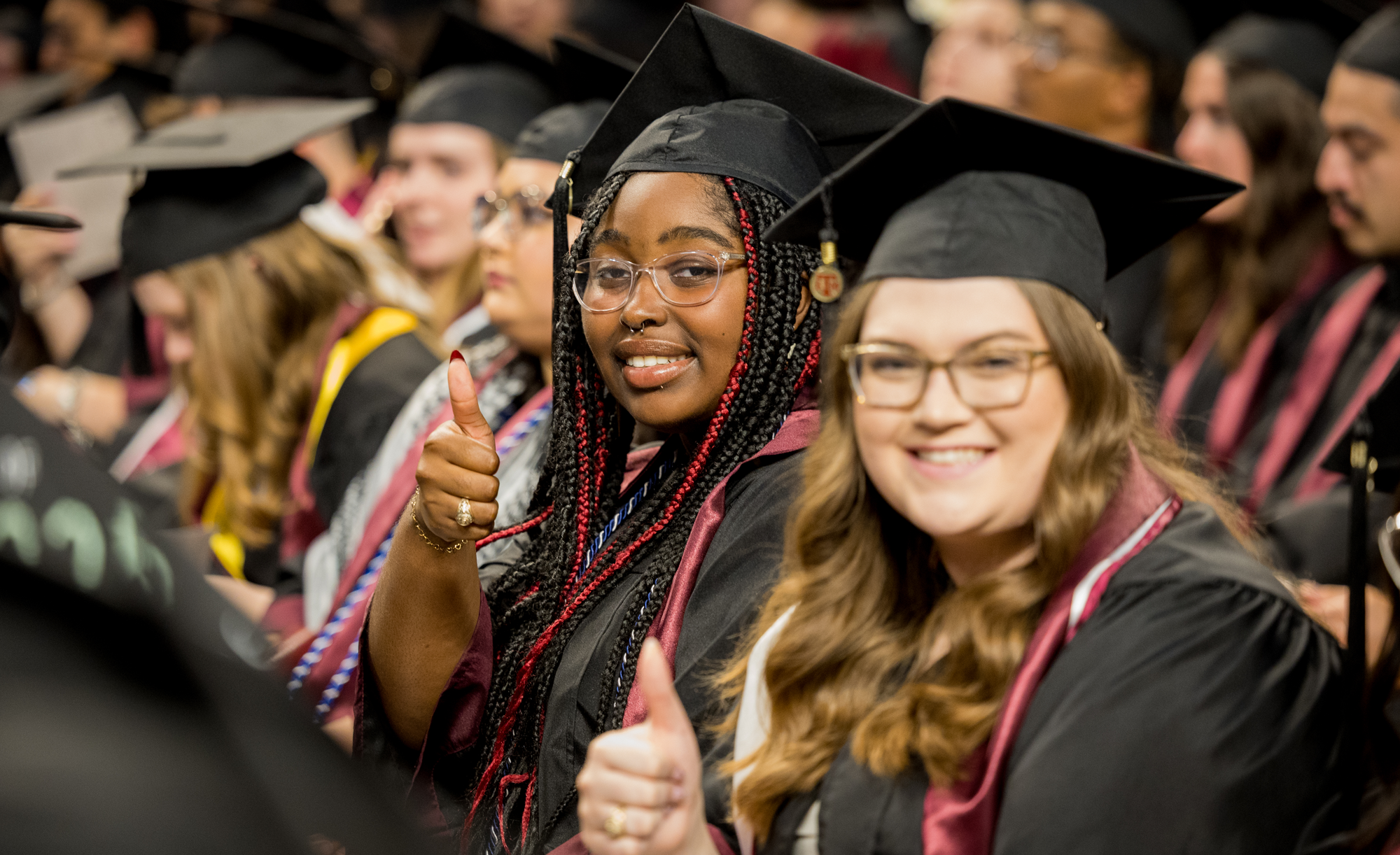 Graduates in caps and gowns giving a thumbs up at a graduation ceremony.