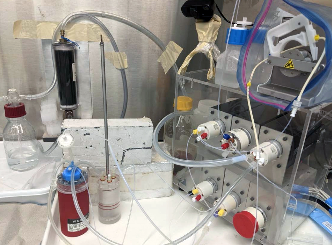 Laboratory equipment setup featuring tubes, glass containers, and a mechanical device with dials and valves used to purify and separate astatine.