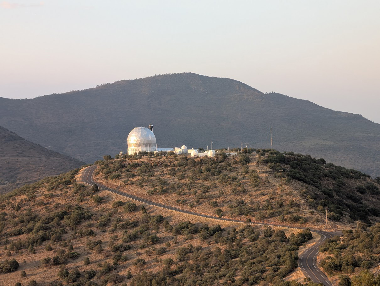 Observatory dome atop a hill surrounded by sparse vegetation, with a winding road leading up to the facility.