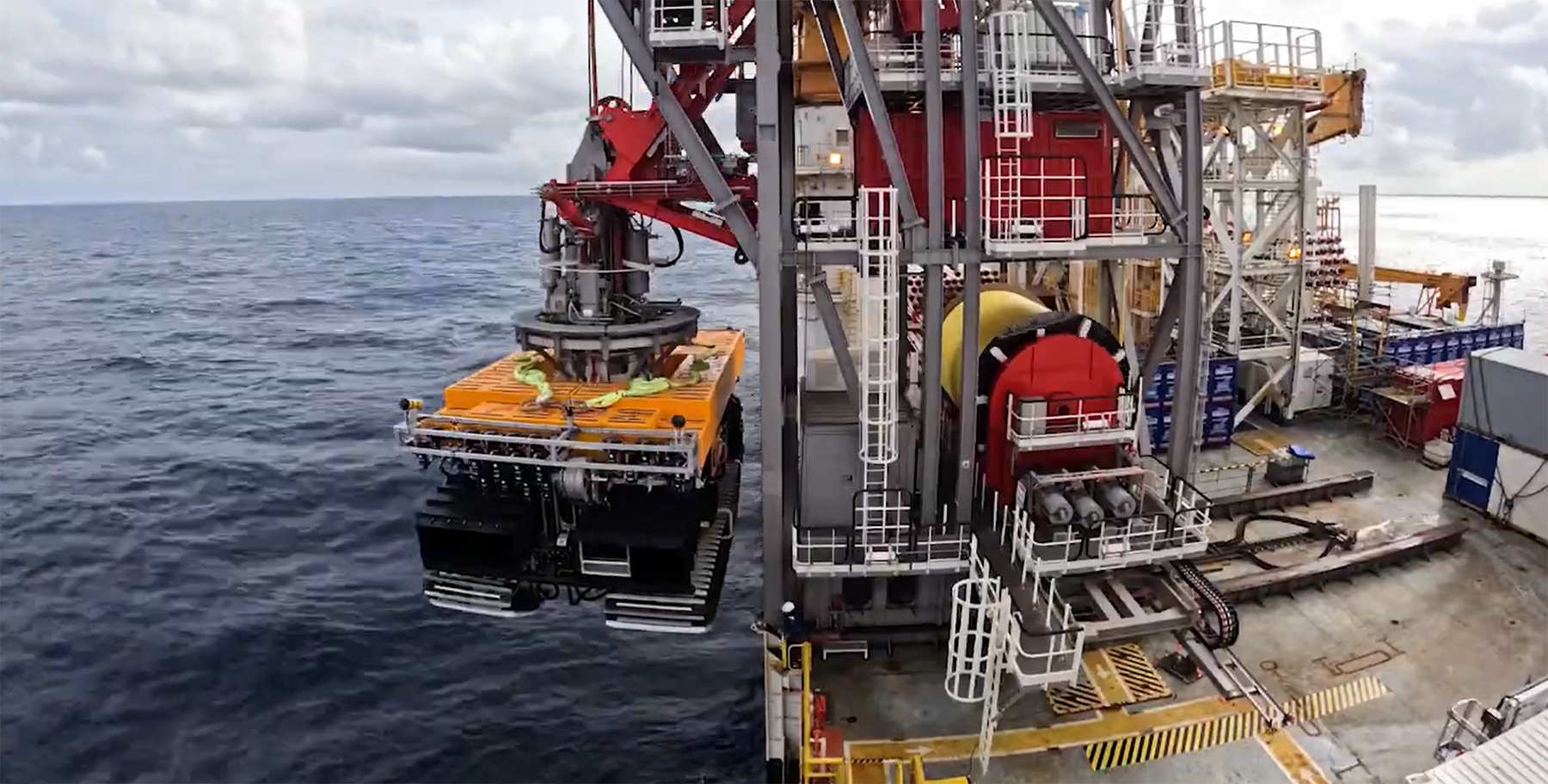 An offshore platform crane lifting a large, orange industrial submersible vehicle above the ocean.