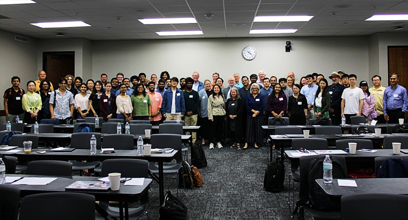 A group of people posing for a photo in a classroom setting at a conference or meeting.