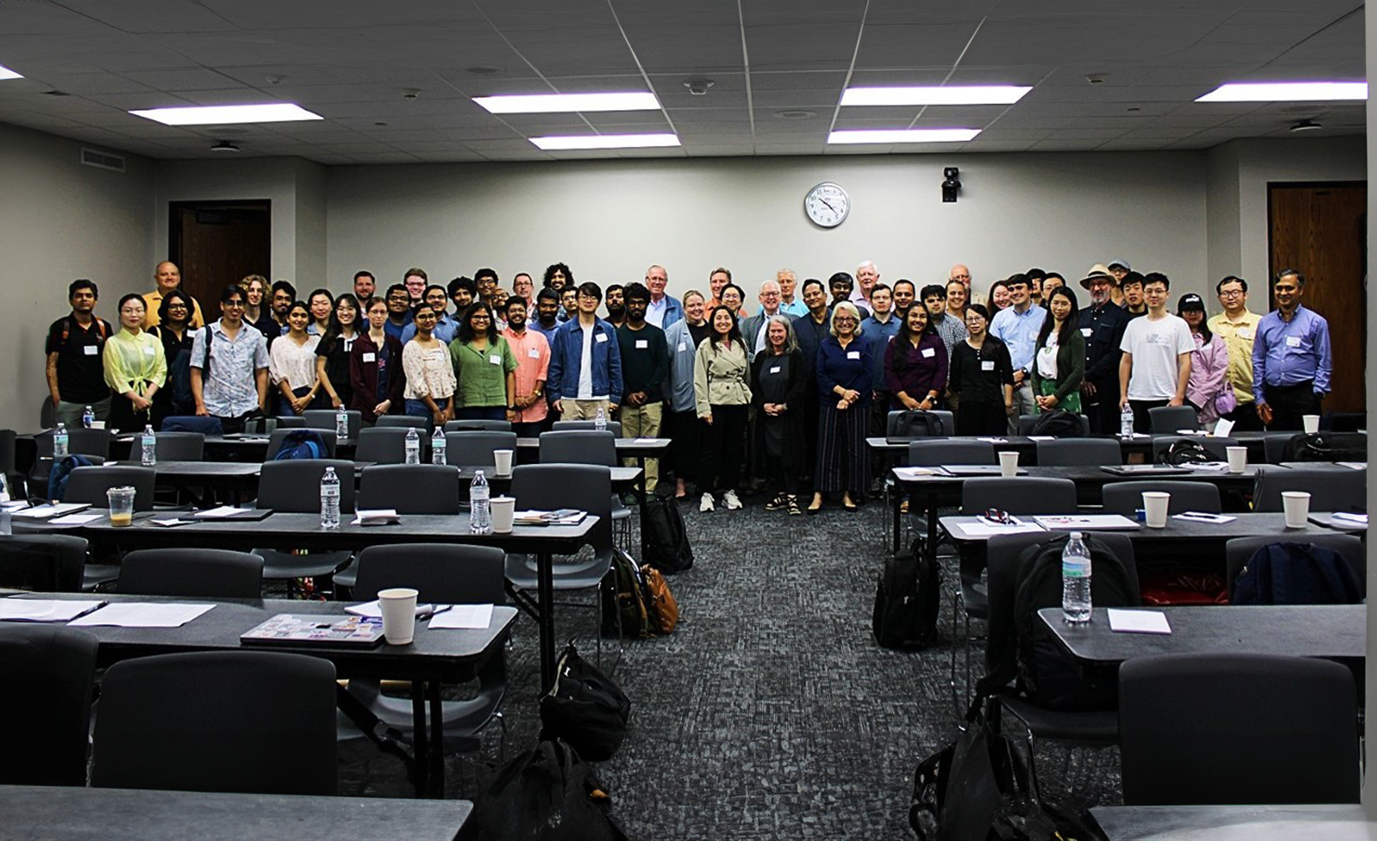 A group of people posing for a photo in a classroom setting at a conference or meeting.