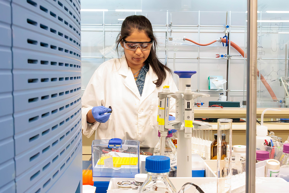 A scientist in a lab coat and gloves is conducting an experiment in a laboratory equipped with various scientific instruments and supplies.
