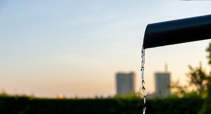 Water flowing from a pipe with a cityscape and sunset in the background.