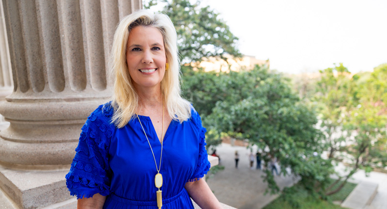 Image of a blonde woman in a blue dress on a balcony overlooking the Century Tree, in front of a concrete pillar with her hand on the railing.
