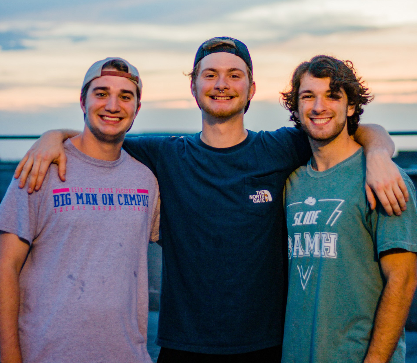 Three college students pose and smile on the beach in the morning hours.
