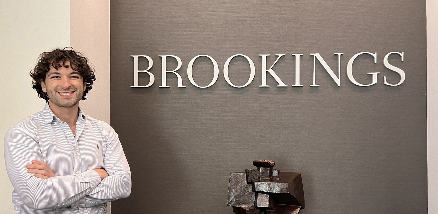 Eric stands in front of the Brookings sign, arms crossed and smiling.
