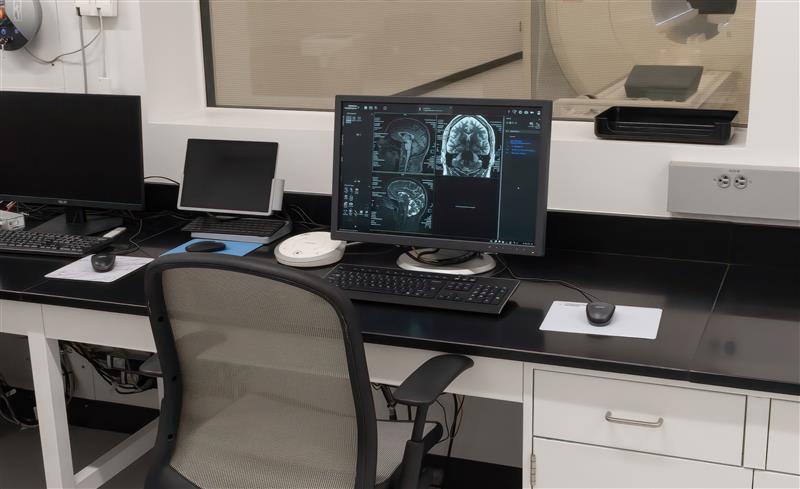 A medical imaging workstation with multiple monitors displaying brain scans, located in a well-equipped office setting.