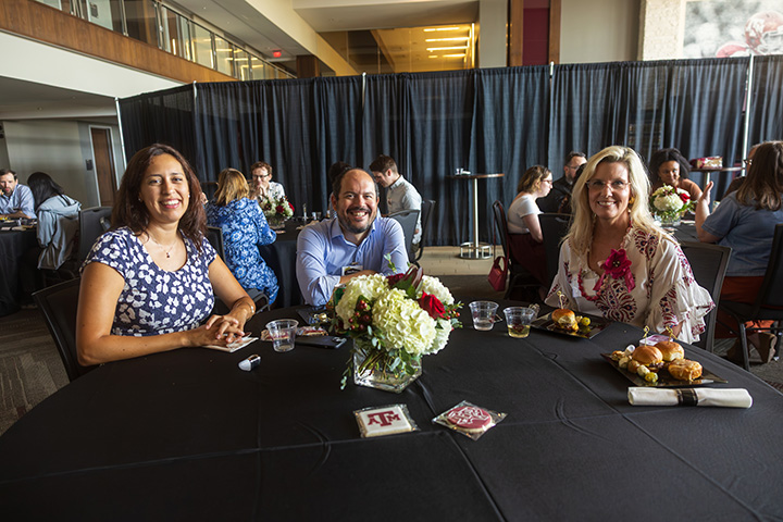 Three faculty members sit around a table with a black table cloth, smiling and chatting.