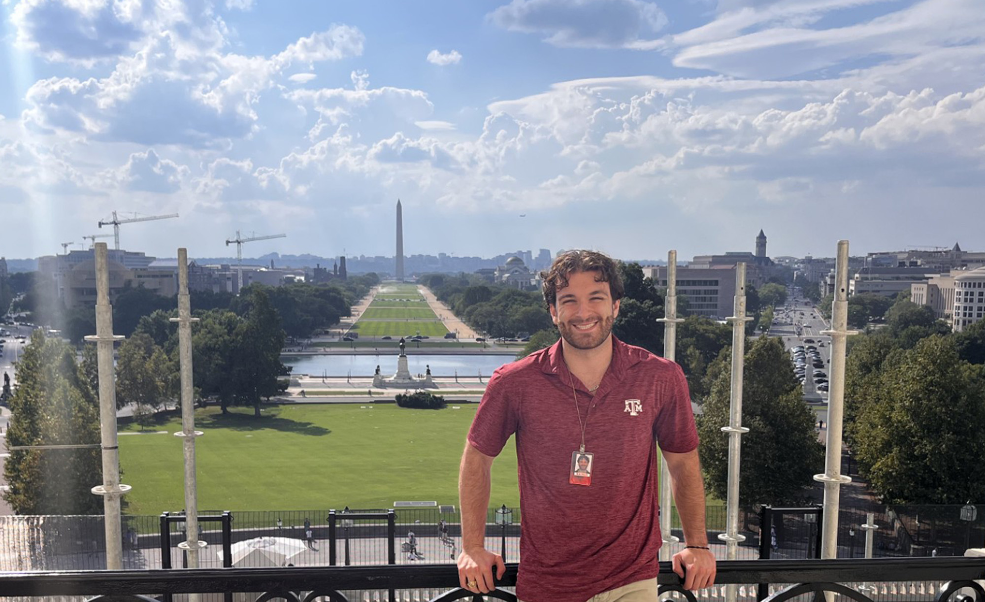 Person standing on a balcony with a scenic view of the National Mall, featuring the Washington Monument in the background, on a sunny day.