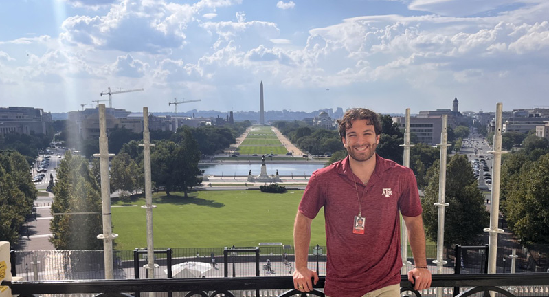 Person standing on a balcony with a scenic view of the National Mall, featuring the Washington Monument in the background, on a sunny day.
