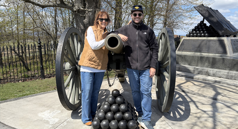Woman and man Dayna Boren Cartwright and Nick Cartwright standing on either side of a canon with a stack of cannonballs in the foreground