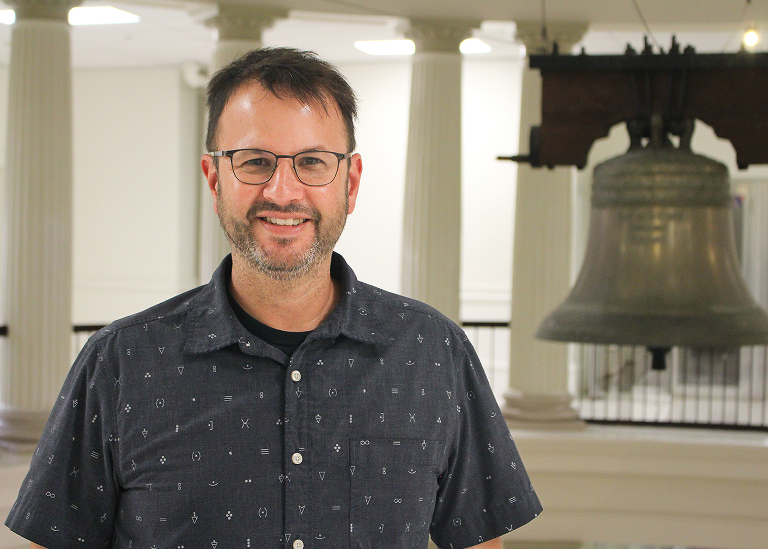 Joshua Hicks standing with the bell in the Academic Building in the background