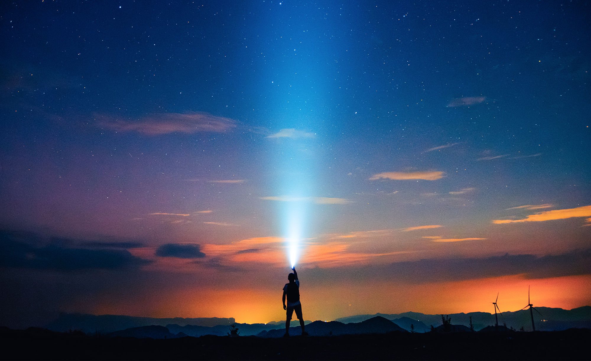 A person standing outside pointing a flashlight into the night sky