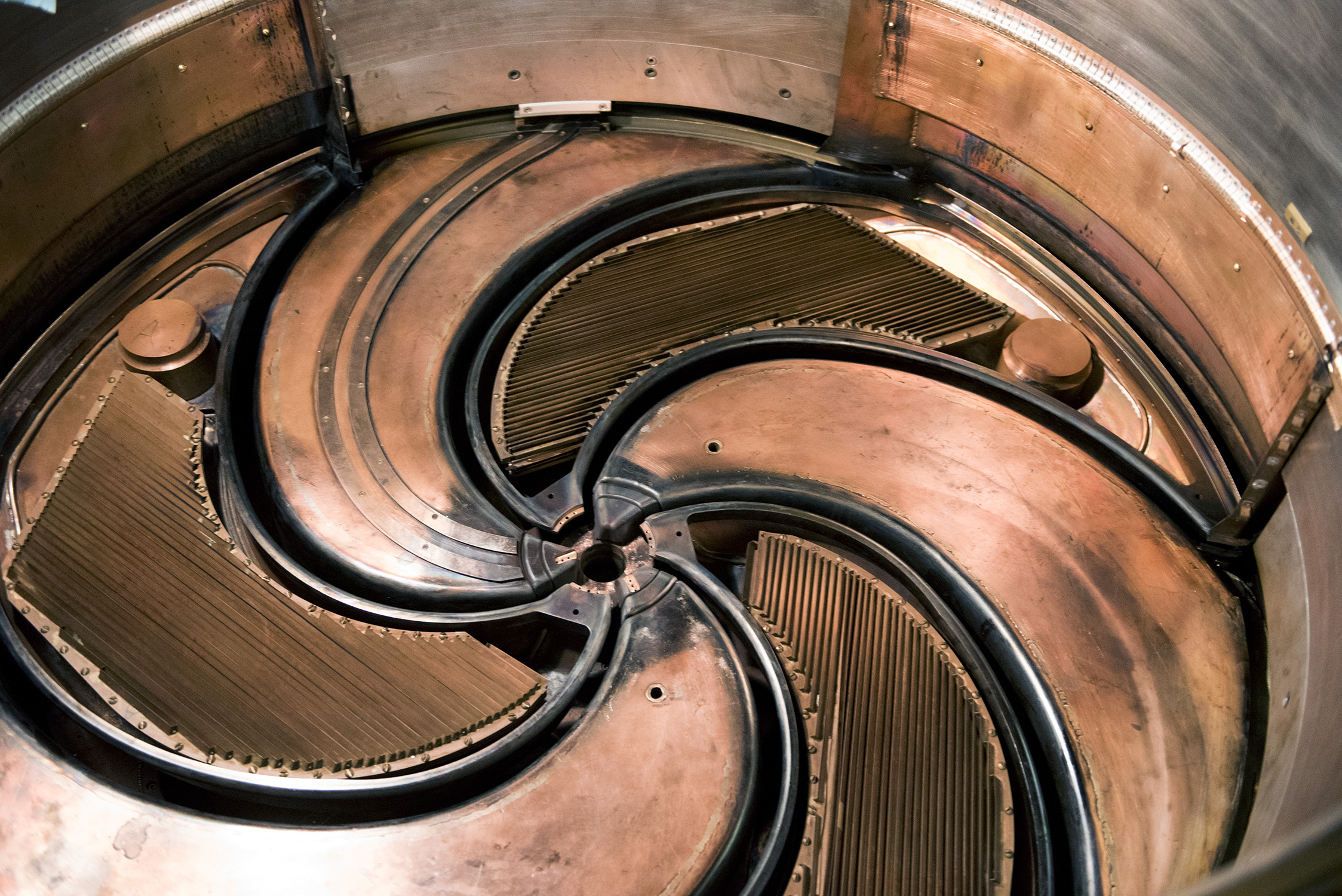 Close-up of the K500 superconducting cyclotron — a circular, copper-colored turbine rotor with intricate grooves and curved vanes — within the Cyclotron Institute at Texas A&amp;M University.