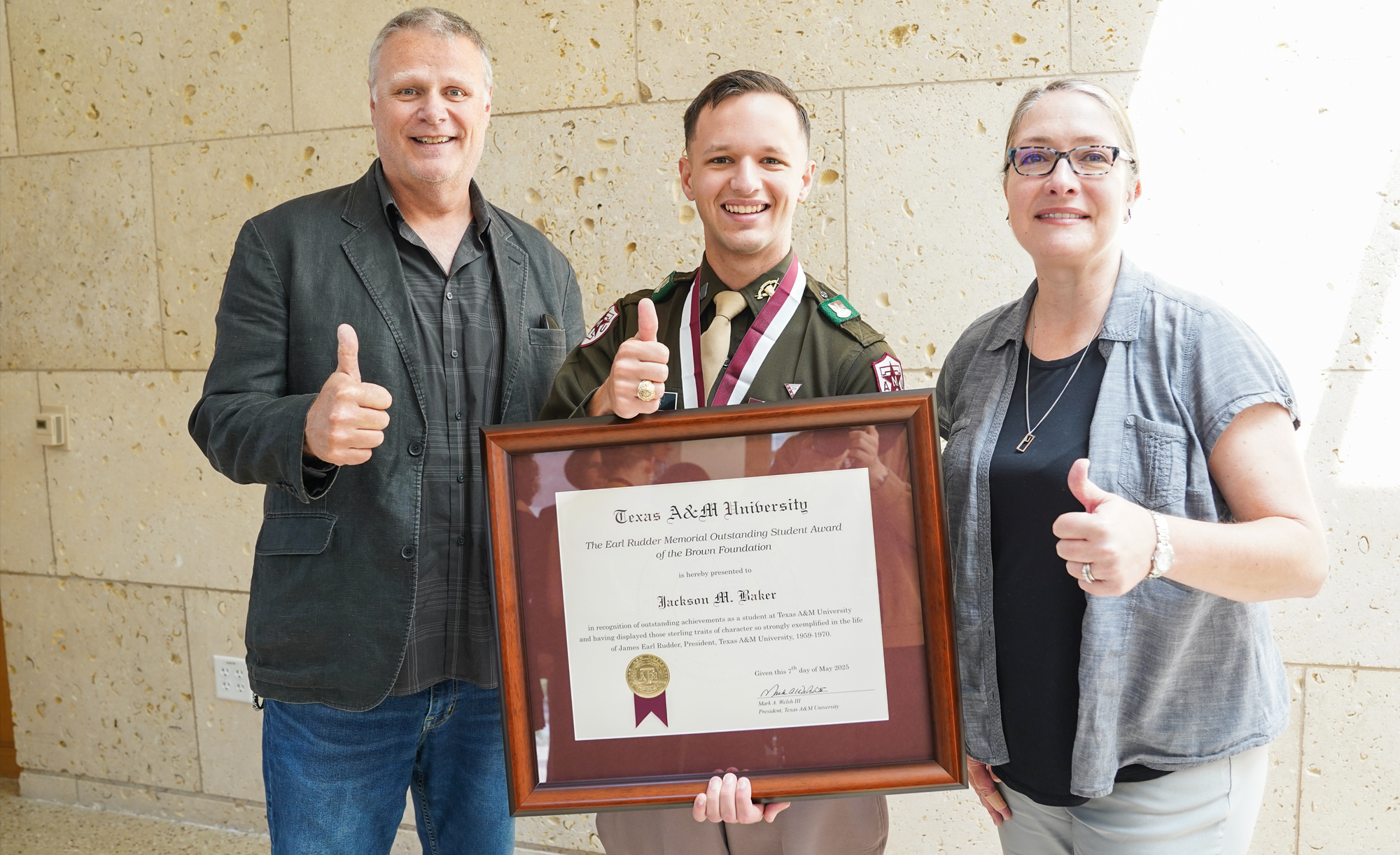 Dr. Darryl De Ruiter, Jackson Baker, and Dr. Angela P. Hudson pose for a photo, with Baker holding a framed award certificate. All three are giving a thumbs-up.