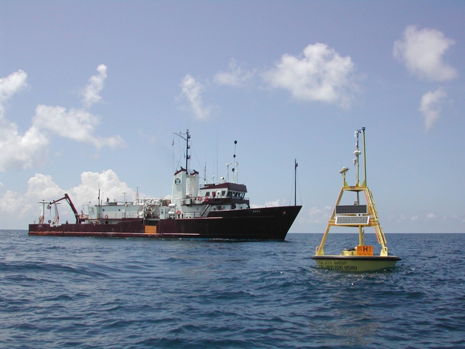 A mid-sized ship is seen in the ocean conducting research with a solar-powered buoy in the water.