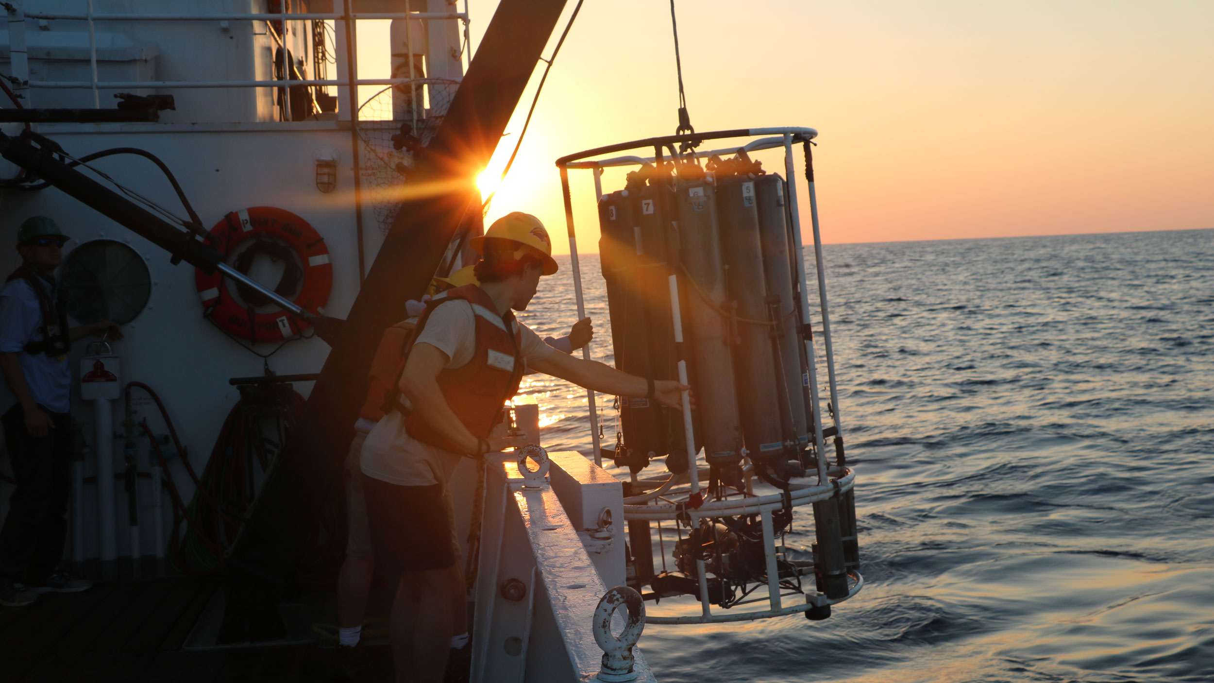 Two student researchers pulling up research equipment onto a boat from the ocean