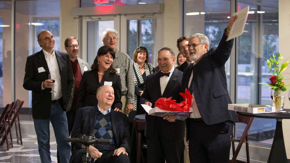 George P. Mitchell celebrating with a group of professors in the Mitchell Institute.