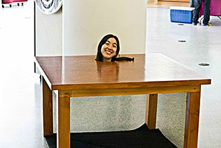 A wood table with a woman's head sticking though a hole on top. Her body is not visible, it appears that is just her head.