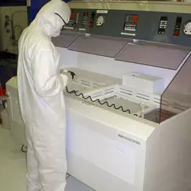 a person in a protective suit covering them from head to toe. Stading in front of a large scientific instrument, holding a tool connected with a coiled wire