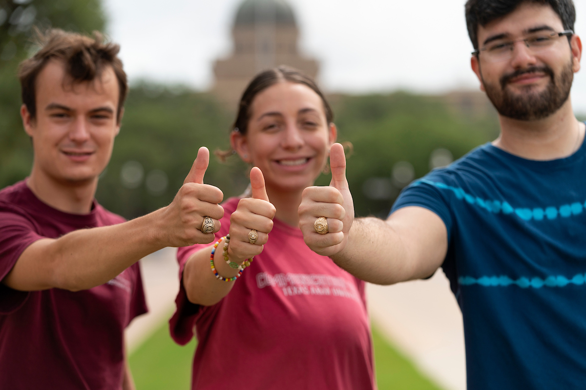 Three students holding thumbs up gesture and displaying their gold Texas A&amp;M class rings to the camera